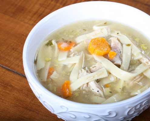 chicken noodle soup in a cream colored bowl ready to eat with large noodles