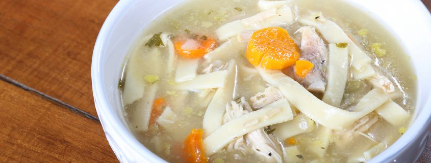 chicken noodle soup in a cream colored bowl ready to eat with large noodles